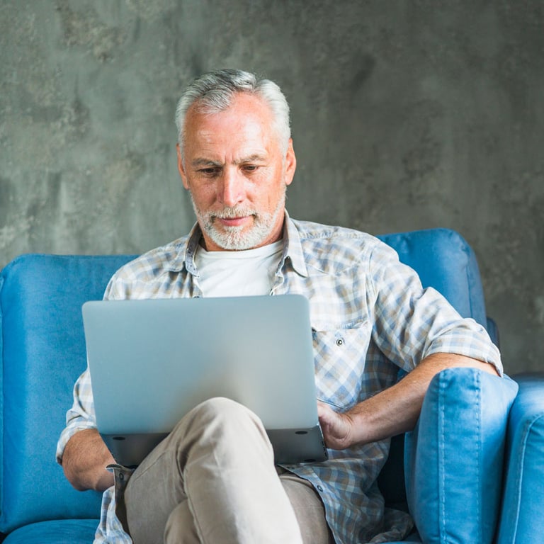 Miembro de Alianza usando su computadora portátil mientras está sentado en su sofá azul para pagar sus facturas.