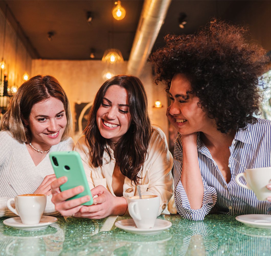 Grupo de chicas pagándose entre ellas en una cafetería usando su celular y opciones de pago de Alianzas